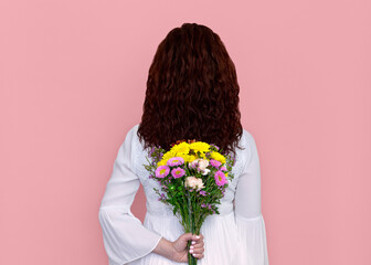 Woman Holding Flowers Behind Her Isolated on Pink Background. Woman Holding Flowers Behind Her Isolated on Pink Background. Back portrait of playful woman in white dress holding bouquet of flowers.