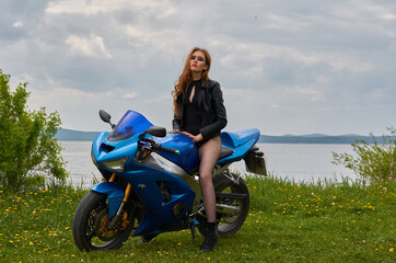 Fototapeta na wymiar a young woman with red hair and wearing a black leather jacket on a blue sports motorcycle