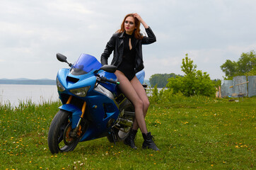 Fototapeta na wymiar a young woman with red hair and wearing a black leather jacket on a blue sports motorcycle