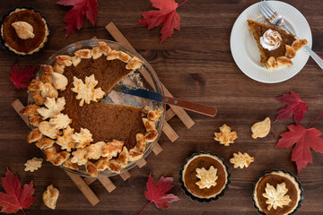 Top down view of a fresh homemade pumpkin pie with one slice on a plate.