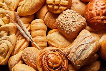 Close up of different types of breads and golden buns with ears of wheat. Food and bakery concept. Salty and sweet food. Bakery and carbohydrates. Horizontal photo.