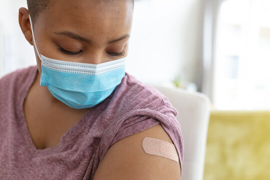 African american plus size woman in face mask showing arm with plaster after vaccination