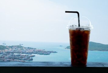 Ice black coffee or iced americano in plastic cup with straw at outdoor coffee shop with freshly day, blue sky and sea port background