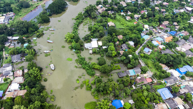 Flood waters overtake a house and rice field at Central of Thailand in 2021. Many buildings are submerged in water. Photo disaster from above view by drone