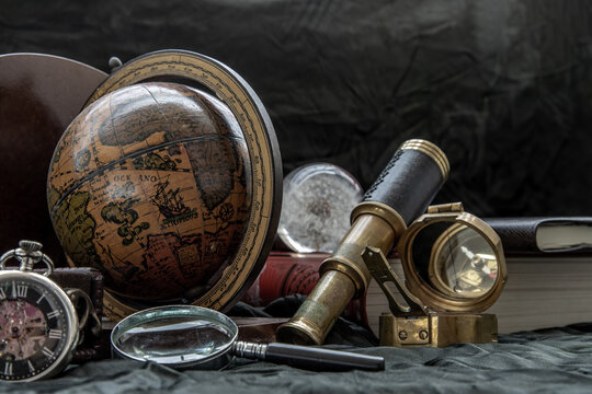 Travel or adventure concept background. Pocket watch, binoculars, antique compass, globe, magnifying glass and stack of books on dark background. Journey Concept, Vintage Style. Selective focus.