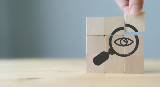 Search, Research, Finding Solution, Investigate Concept. Hand holds the wooden cubes with magnifying glass with eye symbols on grey background, copy space. Marketing research. Customer insight.