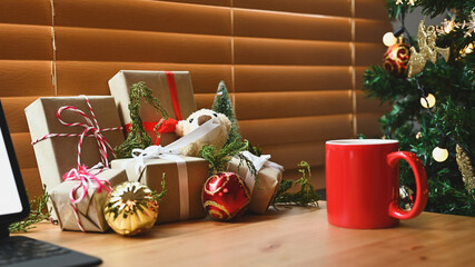 Red cup of hot beverage and Christmas presents on wooden table.