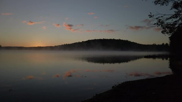 Magic hour wide shot of a dawn mist moving over MacDonald Lake in Haliburton Forest