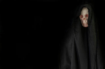 human skull in black hood in the dark