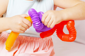 The child plays a pop tube of different colors. Pop tube yellow, purple, red. Macro shooting. The girl stretches and changes the shape of the corrugated tube