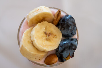 top view of a dairy dessert with banana, almond and plum in a glass