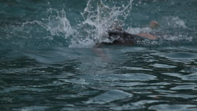 Caucasian man swimming freestyle in water, slow motion, towards camera