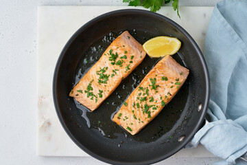 Tasty juicy and flavorful salmon fillet fried on pan with parsley, oil and lemon. Pescetarian lunch. Healthy and dietary fish dish full of omega and fats. Top view, copy space, horizontal