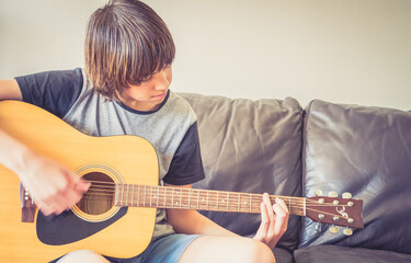 Mixed Race Teenage Boy Practicing Playing the Guitar at Home on Couch