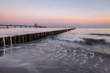 Sunrise at the coast of baltic sea with pier and incoming waves at the groins, Zingst, Western-Pomerania, Germany