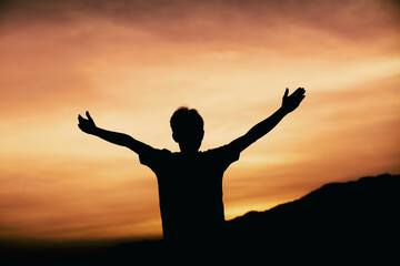Fototapeta na wymiar Man pray with arms stretched out to a sunset sky, christian silhouette concept.