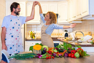 Happy adult couple dance and have fun together in the kitchen at home while preparing healthy...