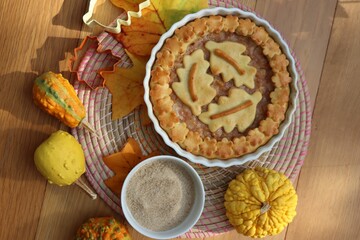 Traditional homemade Apple Pie with fall decoration on a wooden table with ornamental pumpkins and fallen leaves