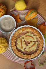 Traditional homemade Apple Pie with fall decoration on a wooden table with ornamental pumpkins and fallen leaves