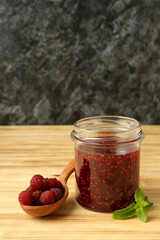 Jar of raspberry jam with ingredients on wooden table