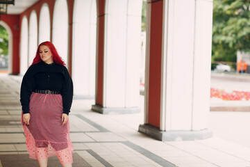 European plus size bold woman walking outdoor street city. Young red pink haired body positive girl.