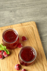 Glass jars of raspberry jam with ingredients on wooden board