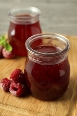 Glass jars of raspberry jam with ingredients on wooden board
