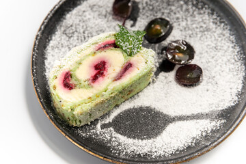 meringue roll on a black round plate powdered with powdered sugar on a white background close up