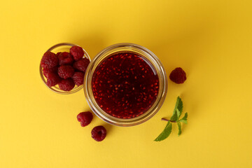 Jar of raspberry jam with ingredients on yellow background
