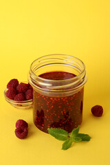 Jar of raspberry jam with ingredients on yellow background