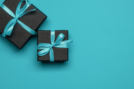 Black gift boxes tied with turquoise ribbons on a turquoise background.