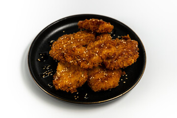 Chicken bytes in Tokyo sauce on a black plate on a white background