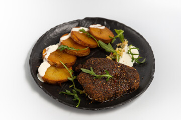 pepper steak with fried potato rings in cream sauce on a black plate on a white background