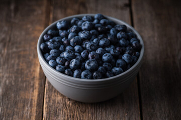 Blueberries in ceramic bowl on rustic wooden background. Selective focus. Shallow depth of field.