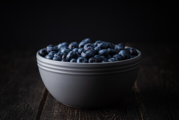 Blueberries in ceramic bowl on rustic wooden background. Selective focus. Shallow depth of field.