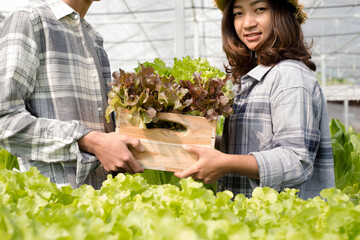 Hydroponics, smiling young Asian couple farmers holding vegetable baskets, standing on a farm, growing organic, commercial organic vegetables. Organic farming business concept