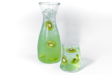 Clear fresh cool kiwi lemonade in a glass and pitcher with ice and kiwi slices isolated on a white background
