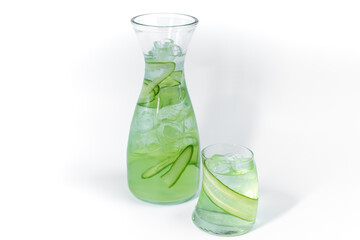 Clear fresh cool cucumber lemonade in a glass and pitcher with ice and cucumber slices isolated on a white background