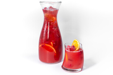 Clear fresh cool berries and orange lemonade in a glass and pitcher with ice and orange slices isolated on a white background