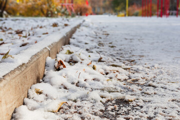 Snow-covered road in the park with fallen leaves. The concept of the first snow in winter or autumn