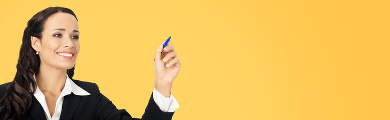 Portrait of happy smiling beautiful young businesswoman in black confident suit, writing or drawing something on screen, by marker. Brunette woman, isolated over yellow color background