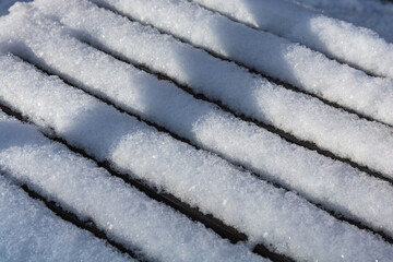 Fresh white snow lies on the bench. Snowy texture