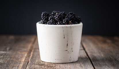 Fototapeta na wymiar Blackberries in ceramic bowl on rustic wooden background. Selective focus. Shallow depth of field.
