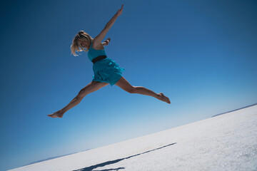 blonde woman dressed in blue jumping a giant leap on a salt lake