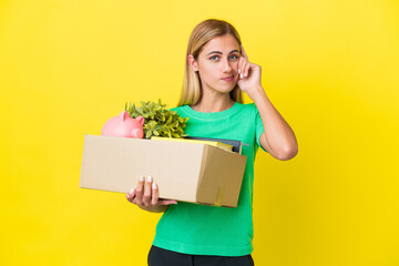 Young Uruguayan girl making a move while picking up a box full of things isolated on yellow...
