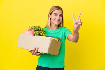 Young Uruguayan girl making a move while picking up a box full of things isolated on yellow...