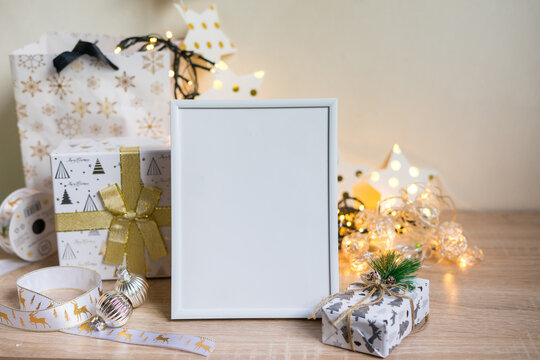 Portrait white picture frame mockup with christmas gifts, boken lights