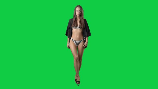 Slow motion of walking young slim attractive woman in bikini and beach tunic. Full body on green screen chroma key background