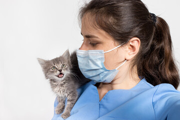A veterinarian in a protective mask and uniform and a small gray kitten. Hospital for animals, treatment of pets.