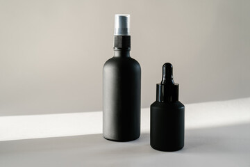 Black cosmetic bottles on a background flooded with sunlight.